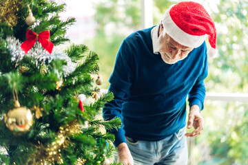 Senior man relaxing decorating christmas tree and smiling while celebrating new year eve and enjoying spending time together in christmas time at home