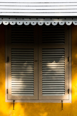 Closed wooden window on yellow dirty wall with awning