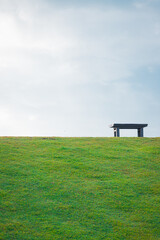 Bench over the green grass field against the sky. Feel empty but peaceful