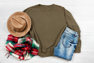 Sweatshirt mockup. Template blank khaki shirt top view on white wooden background. Winter outfit on wood floor. Woman fashion clothes. Spring look of today. Female Jeans, hat, scarf accessories