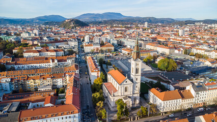 Fototapeta na wymiar Aerial view of Graz city in the austrian region Styria with a church in the foreground and the inner city with the Schloßberg landmark in the background