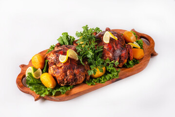 two fried chicken with potatoes, herbs and lemon on a wooden platter on a white background