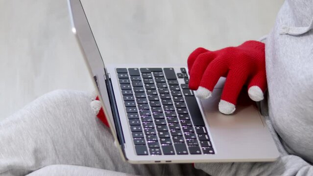 woman in red christmas gloves on keyboard laptop top or side view.female business freelancer sitting on floor social media communication online shopping sale orders.touchscreen gloves compatible