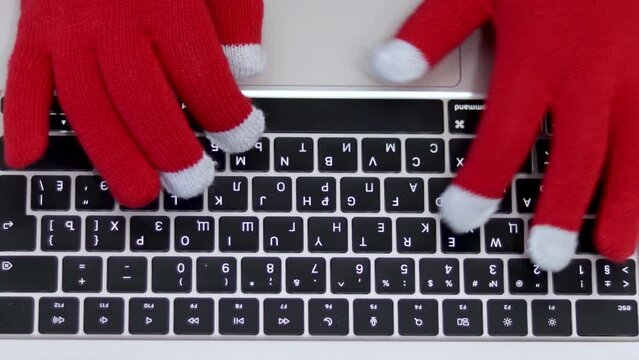 woman in red christmas gloves on keyboard laptop top or side view.female business freelancer sitting on floor social media communication online shopping sale orders.touchscreen gloves compatible