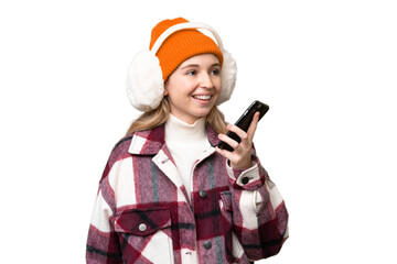 Young  English woman wearing winter muffs over isolated background keeping a conversation with the mobile phone