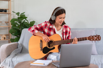 Concept of relaxation with music, Young woman plays acoustic guitar while learning music on laptop