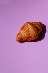 Fresh and delicious croissant on a creative purple background with space for text. Aromatic pastries for breakfast. Stylish concept for bakery and coffee shop