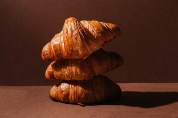 Three fragrant, soft and fresh croissants on a brown background. Monochrome baking concept....