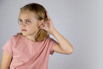 Portrait of a little blonde girl with her palm to her ear, she wants to hear or eavesdrop on something