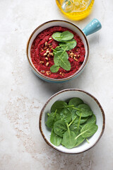 Bowls with beetroot caviar and fresh spinach leaves on a beige stone background, high angle view, vertical shot