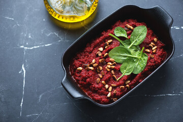 Beetroot caviar topped with spinach and pine nuts in a black serving pan, high angle view on a black marble background, horizontal shot
