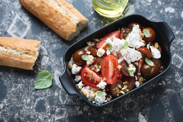 Salad with red tomatoes, ricotta and pistachios on a dark-brown granite background, high angle view, horizontal shot