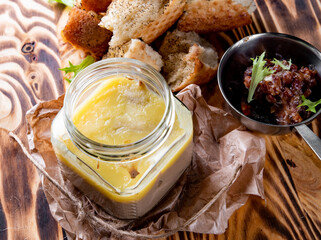 Glass jars of chicken liver pate with sliced bread on wooden table