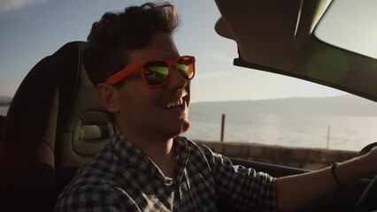 A young men in a shirt rides a convertible along the seashore in the mountains, singing with joy. vacation, car purchase and car rental