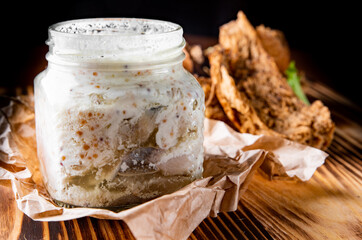 Sliced herring in sour cream sauce served in a glass jar with bread on wooden table