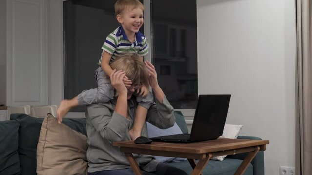 Single mother woman online works at home with laptop at quarantine and same time performs parental duties with playful hyperactive child. Kid sits on neck mom, interfere or distracting to working