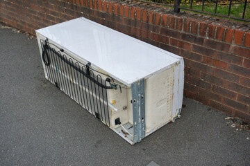 discarded fridge freezer dumped on public path in city. white goods from kitchen illegally thrown...