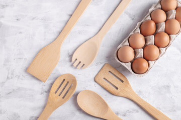 Wooden cooking tools and chicken eggs on gray background, top view. Organic farm products. Home baking concept