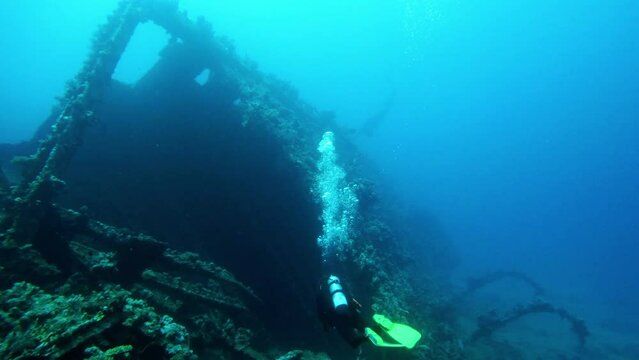 Diver exploring old sunken vessel underwater, back view. Ocean bottom scuba diving, ship undersea, shipwreck discovery in sea, slow motion