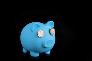 Blue piggy bank with 1 English pound coins instead of eyes on a black background
