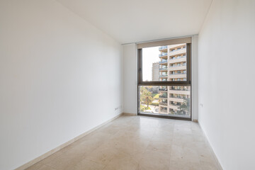 An empty spacious white square room with a large floor-to-ceiling brown framed plastic window. The floor is made of beige impact-resistant ceramic tiles. Lack of furniture in the room.