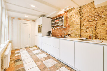 a kitchen area with brick walls and white cupboards on either side, there is a sink in the corner