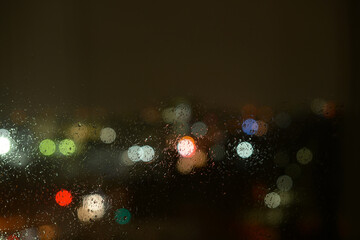 Raindrops on a window glass and unfocused lights of a night or evening city. Background of the...