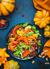 Fresh pumpkin salad with lettuce,  red cabbage, avocado, arugula, pomegranate seeds and nuts. Healthy vegan vegetarian eating, slow comfort food. Blue table background. Top view