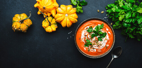 Winter warming spicy pumpkin soup with seeds, cream, pepper and parsley. Healthy comfort slow food. Soup bowl on black table background. Top view banner