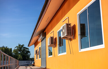 Close-up low-angle view of an orange building with sliding glass windows and an air conditioner compressor.