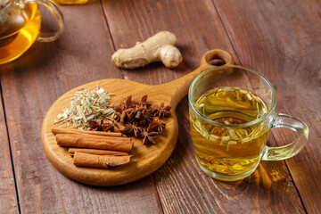 of lemongrass tea on a wooden table set for tea drinking next to anise, lemongrass and cinnamon on a wooden board.