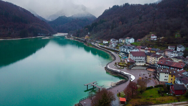 Aerial drone view of the city of Barcis, mountains with snow and fog, emerald lake and autumn trees
