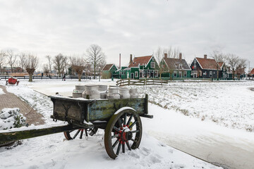An old cart, with milk cans, covered in snow. - 554673156