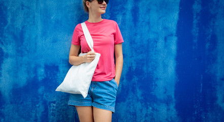 Female model wearing pink blank t-shirt on the background of an blue wall.