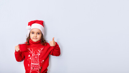 Cute caucasian kid girl in red Santa's hat holding red mug or cup empty copy space for design or text. Banner. Christmas mockup template.