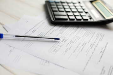 Photo of a pen lying on documents and a calculator in the background