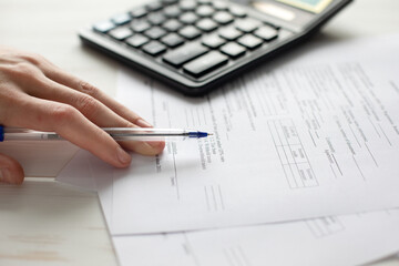 A photo of a person's hand holding a pen and filling out papers. Calculator in the background