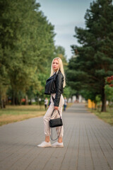 Portrait of a young beautiful blonde girl in a black jacket in the park.