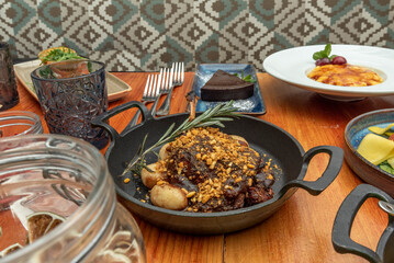 Still life of assorted food dishes featuring a beef stew with potatoes in a cast iron skillet in the foreground