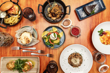 Still life of assorted dishes with braised beef with potatoes in a cast-iron skillet, thick linguine with burrata cheese and basil leaves, chocolate cake, cheesecake