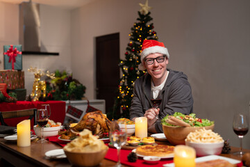 Happy man in glasses wear red Santa Claus hat holding glass of wine while celebrating Christmas dinner with their family.