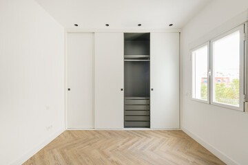 Room with a custom built-in wardrobe with white sliding doors, white painted smooth walls, a gray...