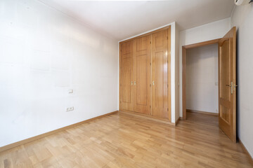 A built-in wardrobe with wooden doors and matching chests in a room with white walls and oak laminate flooring