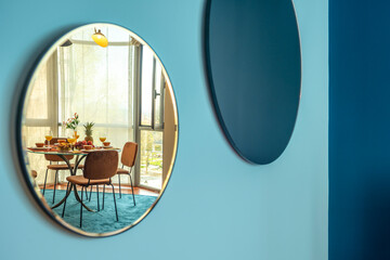 A room with a round mirror on a blue wall reflecting a glass dining table