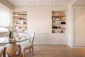 A living room with a wooden bookcase with built-in shelves, white spotlights on the ceiling and a...