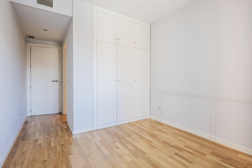 Empty room with a built-in wardrobe with white wooden doors with matching trunks and air conditioning ducts in the false ceiling