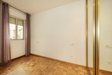 Empty room with built-in wardrobe with gold foil edged mirror doors and window with purple curtains