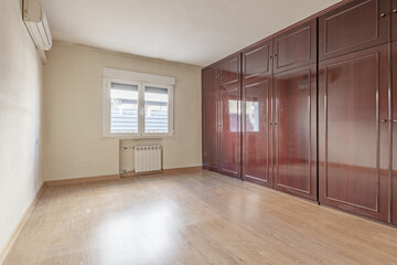 Empty room with built-in wooden wardrobe covering a bright reddish wall