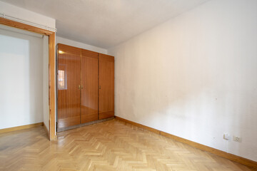 Empty room with old-style glossy wooden wardrobe and French oak parquet floor laid in a herringbone pattern