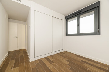 Empty room with a built-in wardrobe with white wooden sliding doors, black anodized aluminum windows and dark stoneware floors